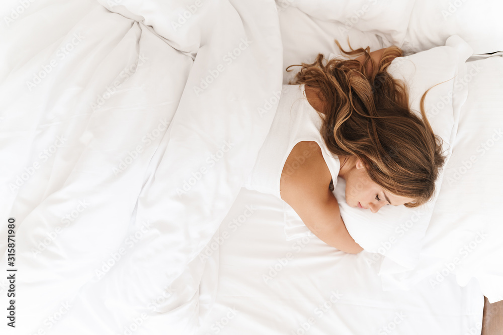 Wall mural Photo of young caucasian woman sleeping and hugging pillow