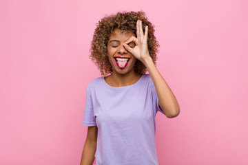 young african american woman smiling happily with funny face, joking and looking through peephole,...