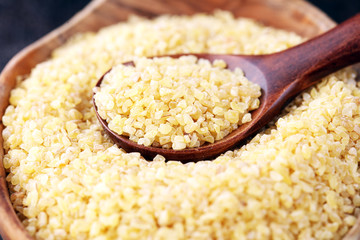 Uncooked bulgur in wooden spoon, rustic style. Healthy Bulgur wheat grains