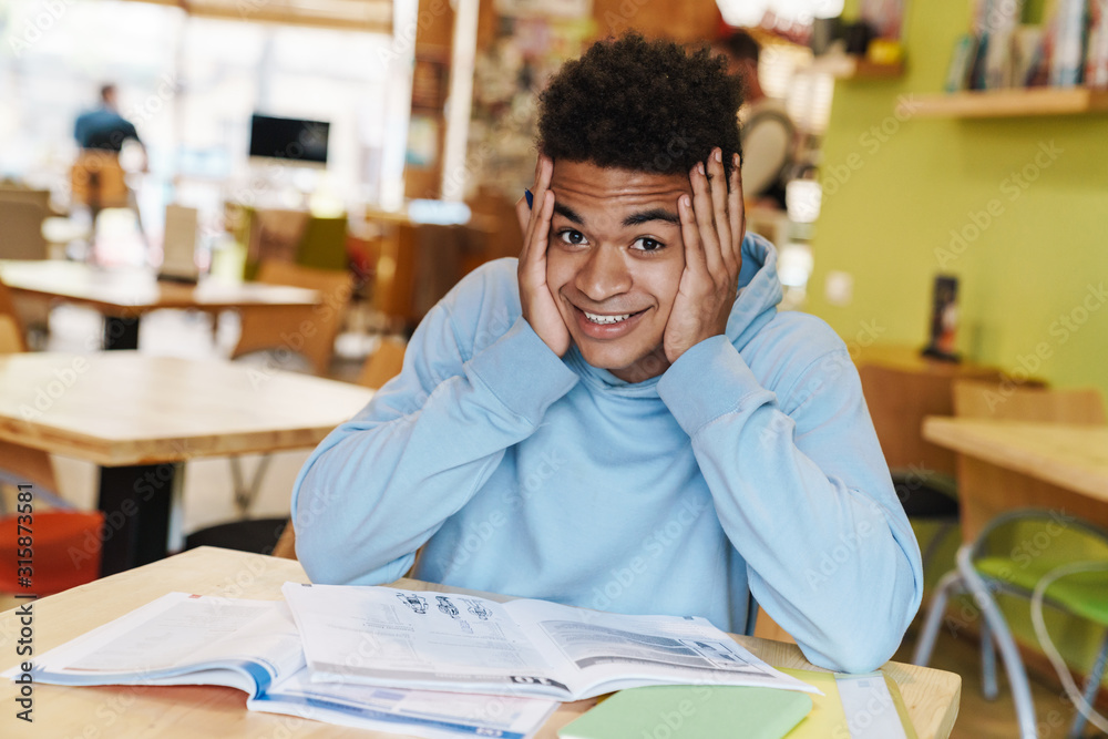 Poster Smiling african bot teenager studying while sitting at the hub