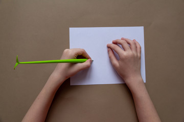 writing left- handed kid one hand with light green pen as sprig are on white paper on craft paper...