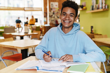 Smiling african bot teenager studying while sitting at the hub