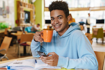 Smiling african bot teenager studying while sitting at the hub