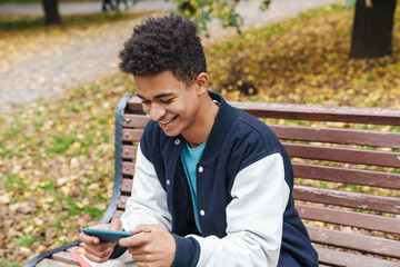 Fototapeta premium Smiling african boy student sitting on a bench at the park