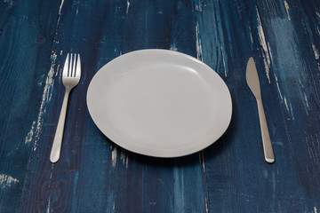 White Plate on blue wooden background with utensils side view
