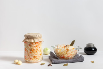 Homemade sauerkraut with carrots in a glass jar and bowl on a white wooden background. Fermented food.
