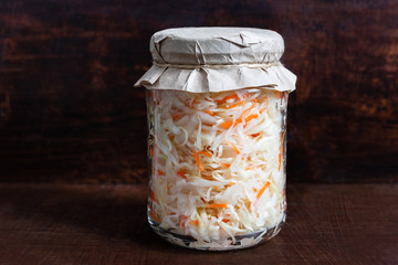 Homemade sauerkraut. Fermented food. Sauerkraut with carrots in a glass jar on a dark wooden background