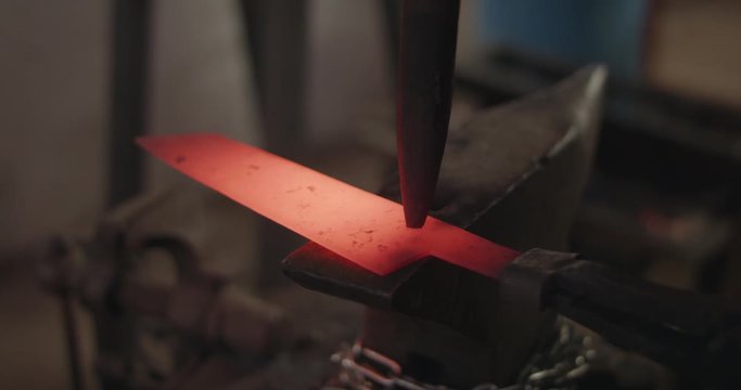 Blacksmith finalizing forging of knife by hammer and chisel engraving macro closeup