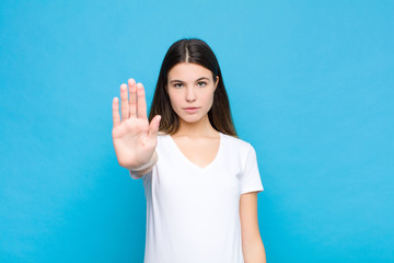 young pretty woman looking serious, stern, displeased and angry showing open palm making stop...