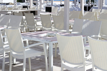 Lots of white tables and chairs arranged on a beach terrace unified in white in a summer resort area