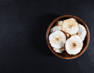 Dried Apple chips in a wooden bowl on a black stone background. Organic natural food.