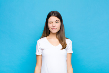 young pretty woman looking happy and friendly, smiling and winking an eye at you with a positive...