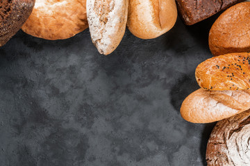 Fresh bakery food, rustic crusty loaves of bread on black stone background. Top view and copy space for text.