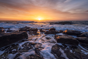 The stunning seascape with the colorful sky and water foam at the rocky coastline of the Black Sea