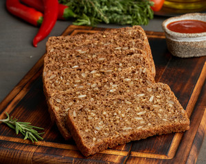 Toasted rye grain bread on a wooden cutting board on dark brown background.