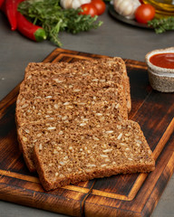 Toasted rye grain bread on a wooden cutting board on dark brown background.