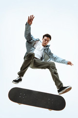 Caucasian young skateboarder riding isolated on a white studio background. Man in casual clothing training, jumping, practicing in motion. Concept of hobby, healthy lifestyle, youth, action, movement.