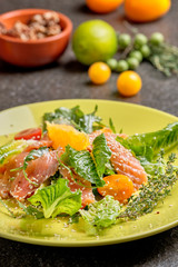 Cold salmon salad with green leaves, cucumber, avocado, lime and tomato on black stone background. Top view with copy space. Rustic style.