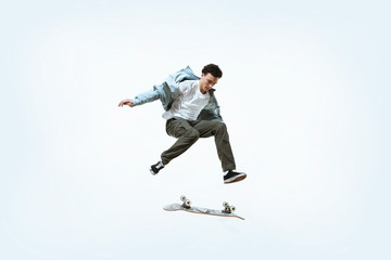 Plakat Caucasian young skateboarder riding isolated on a white studio background. Man in casual clothing training, jumping, practicing in motion. Concept of hobby, healthy lifestyle, youth, action, movement.