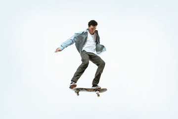 Fototapeta na wymiar Caucasian young skateboarder riding isolated on a white studio background. Man in casual clothing training, jumping, practicing in motion. Concept of hobby, healthy lifestyle, youth, action, movement.