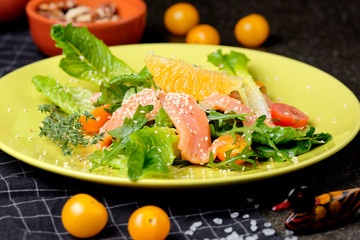 Cold salmon salad with green leaves, cucumber, avocado, lime and tomato on black stone background. Top view with copy space. Rustic style.