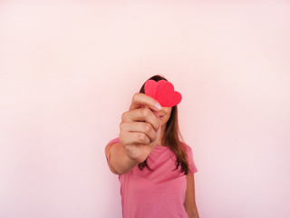 Unrecognizable girl shows to camera heart shape at pink wall at background. Valentines day