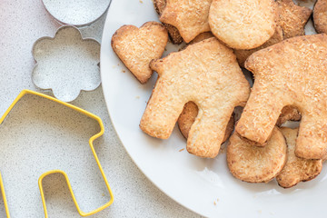 Curly homemade shortbread cookies on a white plate. Rolling pin, forms for cookies on a white table. Top View.