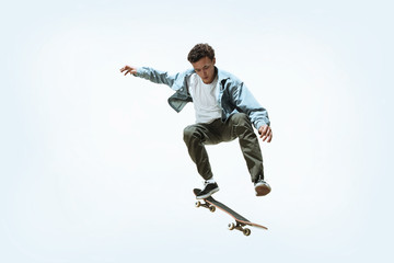 Caucasian young skateboarder riding isolated on a white studio background. Man in casual clothing training, jumping, practicing in motion. Concept of hobby, healthy lifestyle, youth, action, movement.