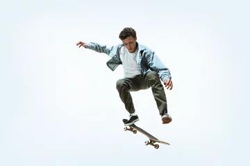 Tuinposter Caucasian young skateboarder riding isolated on a white studio background. Man in casual clothing training, jumping, practicing in motion. Concept of hobby, healthy lifestyle, youth, action, movement. © master1305