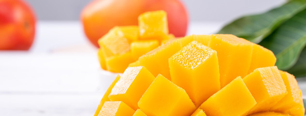 Fresh mango,beautiful chopped fruit with green leaves on bright wooden table background. Tropical fruit design concept, close up, copy space.