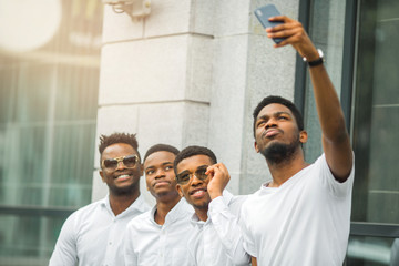 Fototapeta na wymiar four handsome young african men in white shirts are photographed on the phone