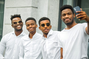 Obraz premium four handsome young african men in white shirts are photographed on the phone