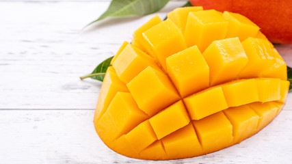 Fresh mango,beautiful chopped fruit with green leaves on bright wooden table background. Tropical fruit design concept, close up, copy space.