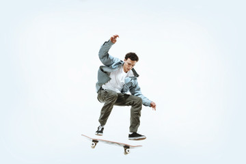 Caucasian young skateboarder riding isolated on a white studio background. Man in casual clothing training, jumping, practicing in motion. Concept of hobby, healthy lifestyle, youth, action, movement. © master1305