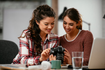 Young woman showing colleague pictures in camera. Two beautiful businesswomen having fun in office. 