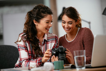 Young woman showing colleague pictures in camera. Two beautiful businesswomen having fun in office. 