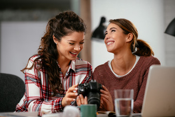 Young woman showing colleague pictures in camera. Two beautiful businesswomen having fun in office. 