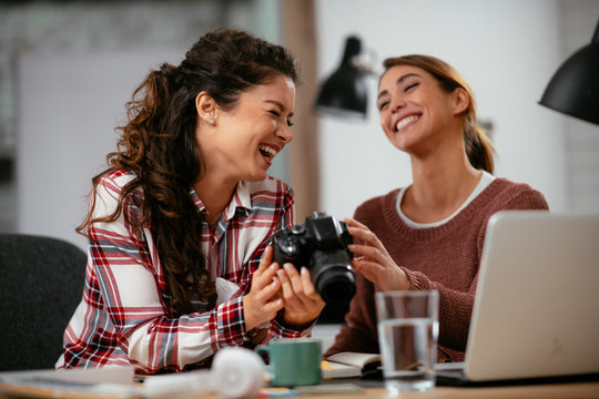 Young woman showing colleague pictures in camera. Two beautiful businesswomen having fun in office. 