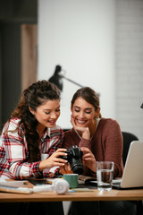 Young woman showing colleague pictures in camera. Two beautiful businesswomen having fun in office. 