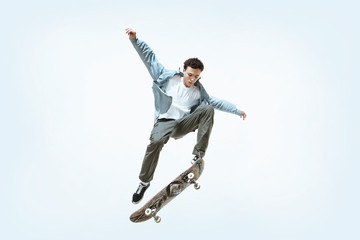 Caucasian young skateboarder riding isolated on a white studio background. Man in casual clothing training, jumping, practicing in motion. Concept of hobby, healthy lifestyle, youth, action, movement. - obrazy, fototapety, plakaty