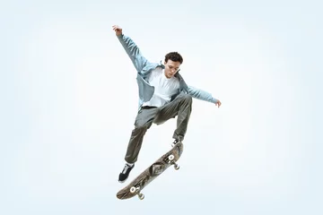 Poster Caucasian young skateboarder riding isolated on a white studio background. Man in casual clothing training, jumping, practicing in motion. Concept of hobby, healthy lifestyle, youth, action, movement. © master1305