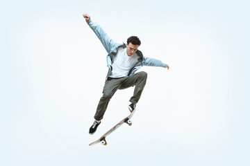 Caucasian young skateboarder riding isolated on a white studio background. Man in casual clothing training, jumping, practicing in motion. Concept of hobby, healthy lifestyle, youth, action, movement. - obrazy, fototapety, plakaty