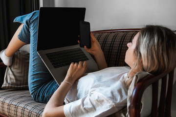 Woman with a laptop is laying on a sofa and using a smartphone. Study and work online, freelance....