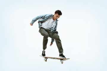 Fototapeta na wymiar Caucasian young skateboarder riding isolated on a white studio background. Man in casual clothing training, jumping, practicing in motion. Concept of hobby, healthy lifestyle, youth, action, movement.