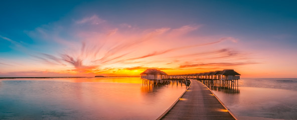 Sunset on Maldives island, luxury water villas resort and wooden pier. Beautiful sky and clouds and...