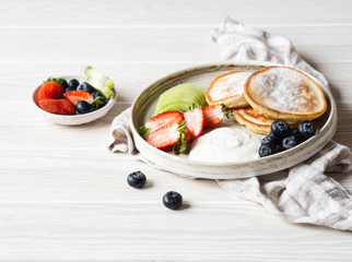 Delicious breakfast - fritters pancakes, sprinkled with powdered sugar with fruits and berries and sour cream on plate on wood table. Copy space
