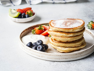 Delicious breakfast - stack fritters pancakes, sprinkled with powdered sugar with fruits and berries and sour cream on plate on wood table.