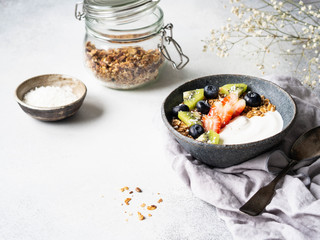 Delicious breakfast - granola with yogurt and berries, dry coconut in bowl and granola in glass jar on the table. Copy space.