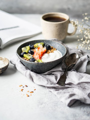 Delicious breakfast - the cup of coffee, dry coconut in bowl, granola with yogurt and berries and open magazine on the table. Copy space.
