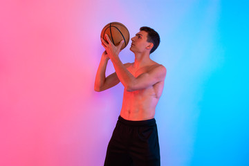 Young athletic man, with basketball, posing on background with neon lights